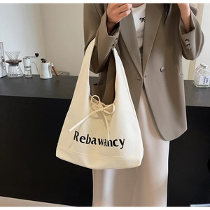 Cream canvas tote bag with bow tie and logo detail shown in a lifestyle cafe setting