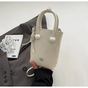 Détail du sac seau en cuir blanc avec poignée à bille et logo métal sur blazer gris