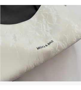 Close-up of ivory shoulder bag showing pleated texture and black brand logo print