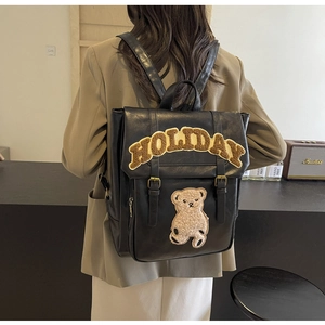 Detail of black leather backpack with plush Holiday lettering and bear patch on a model