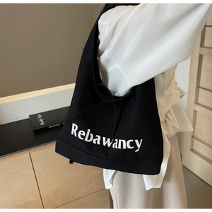 Detail of black canvas tote bag featuring white logo lettering and side bow ribbon accent
