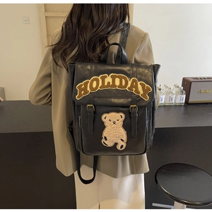 Detail of vintage black PU leather backpack featuring plush bear and Holiday lettering