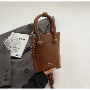 Détail d'un mini sac seau en cuir marron avec lettrage argenté sur un blazer gris