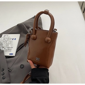 Détail d'un mini sac seau en cuir marron foncé avec logo métallique et pendentif