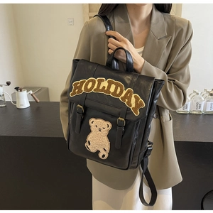 Detail of vintage black leather backpack featuring plush holiday lettering and a teddy bear