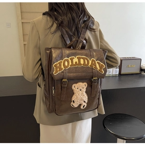Detail of vintage brown leather backpack with yellow Holiday text and teddy bear patch