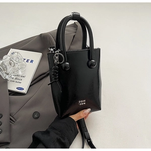 Détail du sac seau noir brillant avec poignée à bille métallique et pompon en cuir