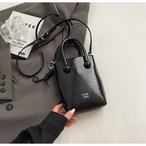 Sac seau en cuir noir brillant avec poignées boules et texte COIH 2DN sur fond de costume