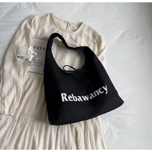 Detail of black canvas tote bag featuring white typography and decorative bow detail