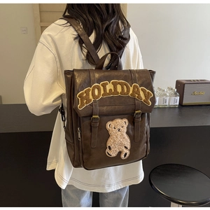 Detail of vintage brown leather backpack featuring holiday patch and teddy bear charm
