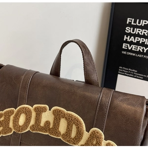 Detail of vintage brown leather backpack with yellow plush HOLIDAY letter embroidery