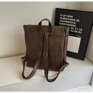 Detail of vintage coffee PU leather backpack straps and adjustable metal buckles on white marble