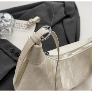 Close-up of cream underarm bag showing crinkled patent leather texture and silver rings