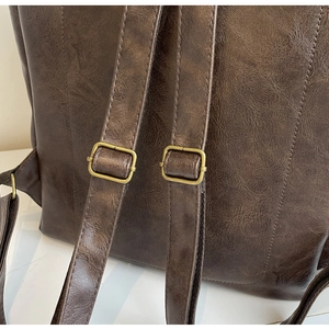 Detail of vintage brown backpack straps with bronze metal buckles and fine stitching