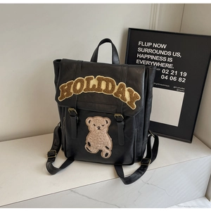 Detail of black faux leather backpack featuring plush holiday lettering and bear patches