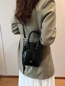 Sac seau noir brillant chic porté par un mannequin avec blazer et jupe blanche