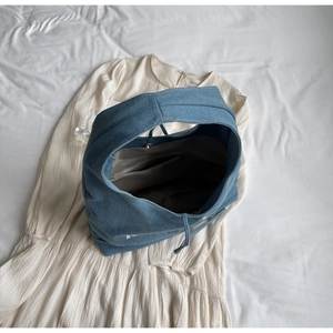 Close-up of a blue denim tote bag with white logo and drawstring details on a white background