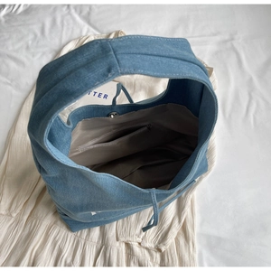 Close-up of denim tote bag showing grey lining, zipper pocket and magnetic snap button