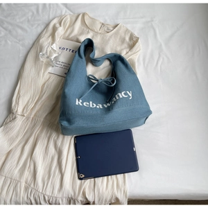 Close-up of large blue denim tote bag with white lettering and drawstring bow detail