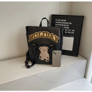 Detail of black PU leather backpack with fuzzy HOLIDAY lettering and a bear patch