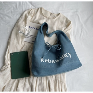 Detail of blue denim tote bag featuring bow drawstring and white Rebawancy letter print