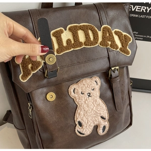 Detail of dark brown leather backpack with plush bear patch and bronze hardware