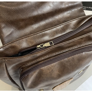 Close-up of double bronze zippers and textured dark brown leather on vintage backpack