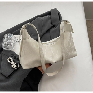 Detailed view of white pleated leather bag with wide strap and embossed brand logo