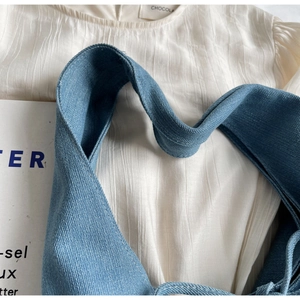 Detailed shot of premium blue denim bag strap against a white striped linen shirt texture