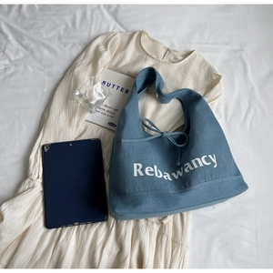 Detail of blue denim tote bag with white Rebawancy lettering and drawstring closure
