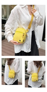 Detail of yellow canvas crossbody bag featuring adjustable strap and front zipper pocket