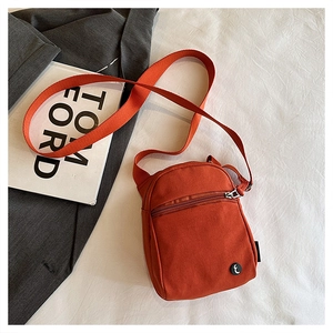 Detail of orange canvas crossbody bag featuring front zipper pocket and round logo patch
