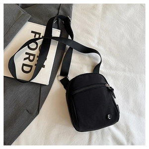 Detail of a black canvas crossbody bag with adjustable strap and front zipper pocket