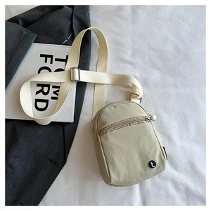 Detail of light olive nylon crossbody bag featuring double zippers and a circular logo