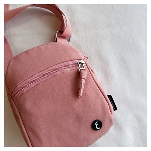 Detail of pink nylon crossbody bag featuring front zipper pocket and adjustable strap