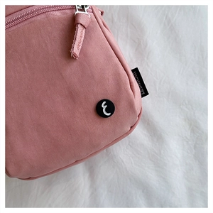 Close-up of pink nylon crossbody bag featuring round black emblem and side brand label