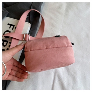 Detail of pink canvas crossbody bag with metal buckle and adjustable fabric shoulder strap