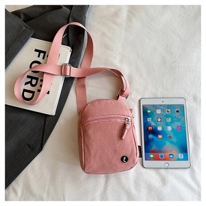Detail of pink canvas mini crossbody bag with zipper pocket next to a tablet