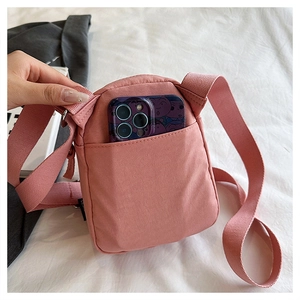 Macro detail of a small light pink nylon crossbody bag with adjustable wide strap