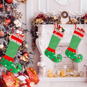 Three green elf Christmas stockings with striped patterns hanging on a fireplace