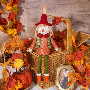 Detail of harvest scarecrow doll with red hat sitting among pumpkins and maple leaves