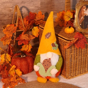 Detail of plush gnome holding corn with fall maple leaves and pumpkin decoration
