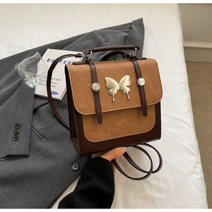Detail of vintage dual-tone leather backpack with silver butterfly accent and top handle