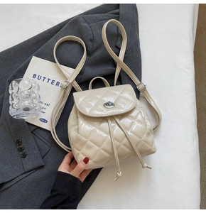 Detail of cream quilted mini backpack with silver twist lock on grey blazer background