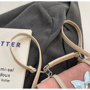 Detail of a pink suede handbag with a light blue metallic butterfly clasp and beige strap