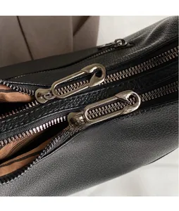 Detail of smooth silver pin-shaped metal zipper pullers on black lychee leather bag