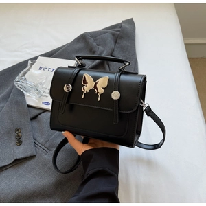Détail d'un sac bandoulière noir avec boucle papillon argentée et poignée chic