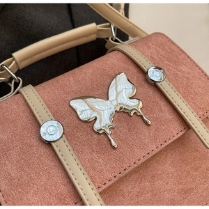 Detail of suede crossbody bag with silver butterfly emblem and contrast stitching