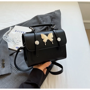 Détail du sac à main en cuir noir avec boucle papillon argentée et bandoulière réglable