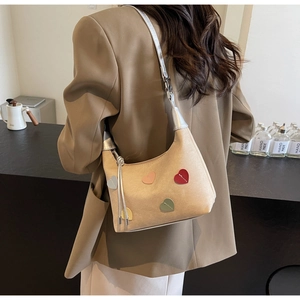 Detail of beige shoulder bag with multi-colored heart patches and silver strap design